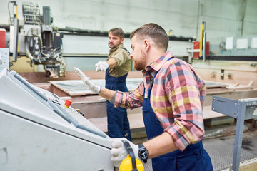 Side view portrait of modern machine operator pressing big red STOP button on control panel in...