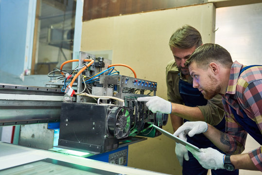 Portrait of two mechanics repairing modern laser equipment in workshop, inspecting operating parts and mechanism, copy space