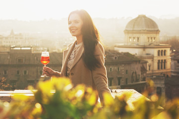 Young woman standing with traditional italian alcohol drink spritz aperol on the terrace with great...