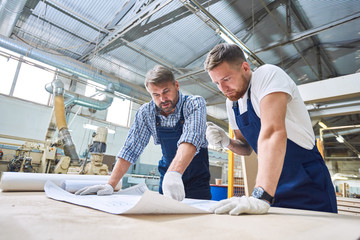 Low angle portrait of two workmen discussing project plans  in workshop of modern  industrial factory, copy space