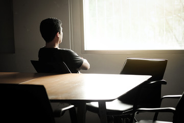 Asian men are thinking in the dark corner of the meeting room and looking out.