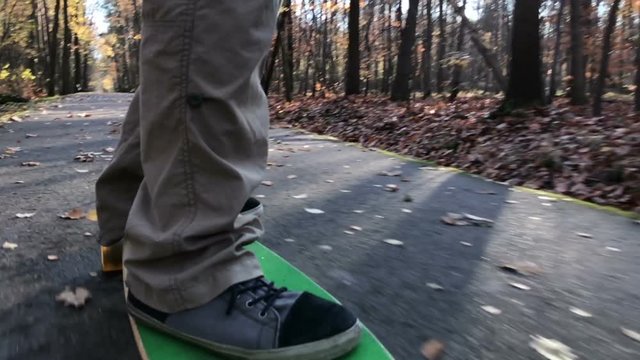 Man skating longboard on the leafs covered path.