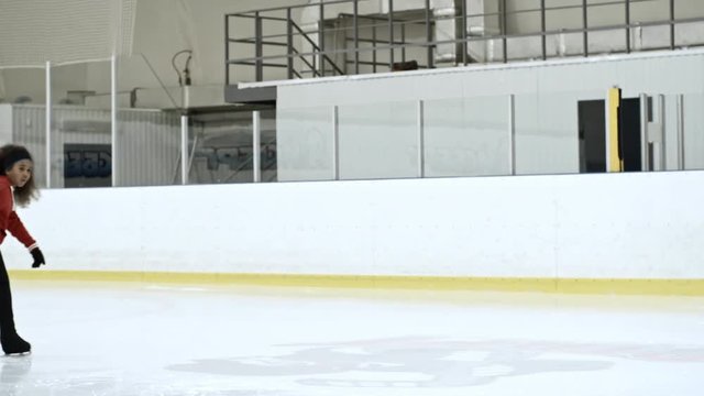 Little African girl training figure skating on ice rink with experienced female coach