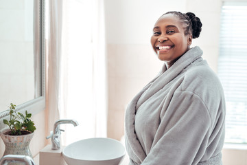 Smiling African woman standing in her bathroom wearing a robe