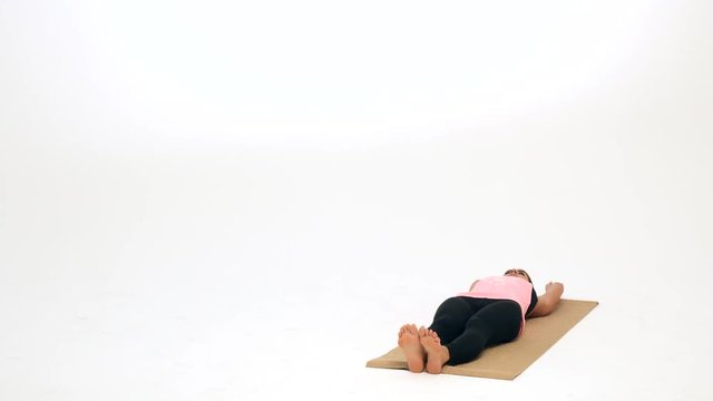 Woman demonstrates stretching exercises and yoga poses on a yoga mat against a white background. She is showing a shoulder stand with legs extended over her head.