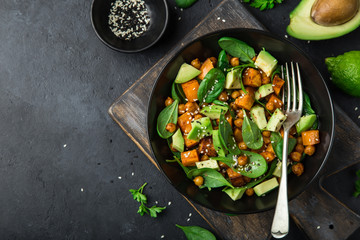  Avocado, quinoa, roasted sweet potato, spinach and chickpeas salad in black bowl.