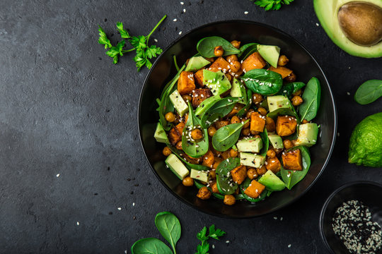  Avocado, quinoa, roasted sweet potato, spinach and chickpeas salad in black bowl.