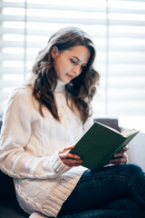 Young beautiful woman reading book at home