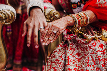 Tender hands of an Indian bride covered with henna tattoo and groom's arm side by side with wedding...