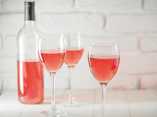 Three wineglass with pink wine and bottle on white brick wall background