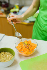 white caucasian woman sprinkles seeds of flax in a glass dish with egg and grated carrots