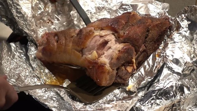 Cook takes out the baked pork leg of the foil. HD video clip