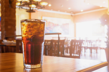 Cola glass with ice on wood table in restaurant background