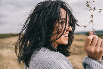 Side view portrait of happy brunette young woman wearing gray sweater being playful and carefree with beautiful smile  and windy hair posing on landscape. Lifestyle concept. Cover idea mood.
