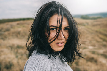 Fototapeta premium Horizontal portrait of romantic brunette woman posing against nature, meadow background with windy hair. People and lifestyle concept. Sensual natural female posing during travel. Cover idea mood.