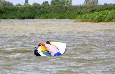 Stand up paddle surfer turns over (drop out) from Stand up paddle board (SUP) into green water of stormy lake - Powered by Adobe