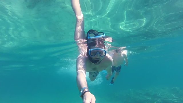 Father and son with fins, mask, snorkel and a selfie stick swimming in the sea, gopro underwater footage