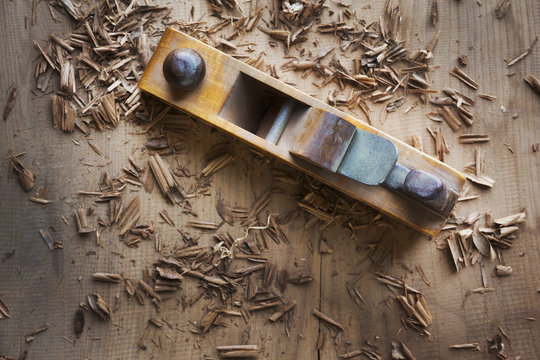 A wood plane on the surface of a piece of wood, shavings scattered about. 