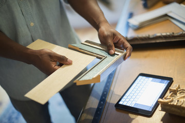 A man holding samples of picture mounts and frames, selecting colour and style. Using a digital tablet.
