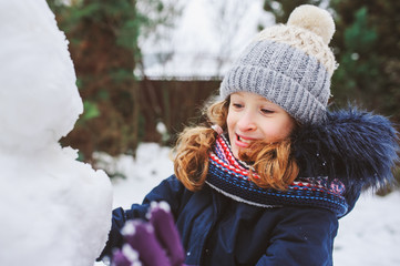 Fototapeta na wymiar happy kid girl making snow man on Christmas vacations on backyard. Winter outdoor activities for kids.