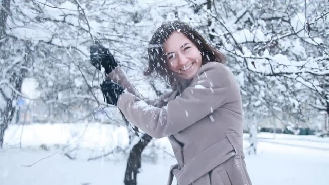 Young girl shakes snow from the tree and smiling on camera outdoors