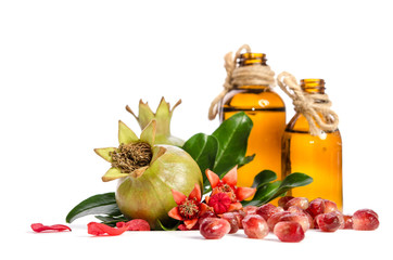  two green pomegranates, bottle with oil and leaves with petals on white background