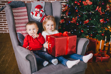 Fototapeta na wymiar Happy cute children posing near Christmas tree in a holiday interior. Little brother and sister in a cozy Christmas room