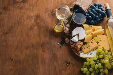 A bottle of wine, and a large assortment of cheeses, honey, nuts and spices, on a wooden table. Top view. Free space for text.