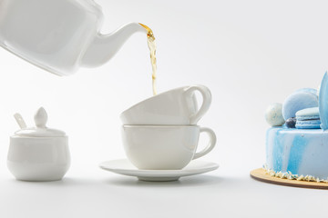 teapot pouring tea in cups near blue cake isolated on white