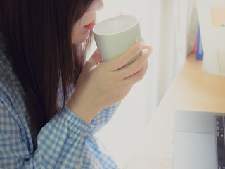 black hair with blue cloth of asian business woman hold cup , drink coffee and working with computer laptop on wooden table background