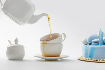 teapot pouring tea in cups near blue cake isolated on white