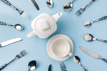 top view of teapot with cup on plate, surrounded by flatware isolated on blue