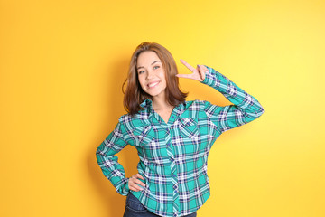 Beautiful smiling woman showing victory gesture on color background