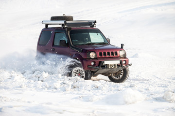 Red japanese SUV riding on snow and snowflakes flying from its wheels