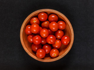 Clay dish with cherry tomatoes on black background