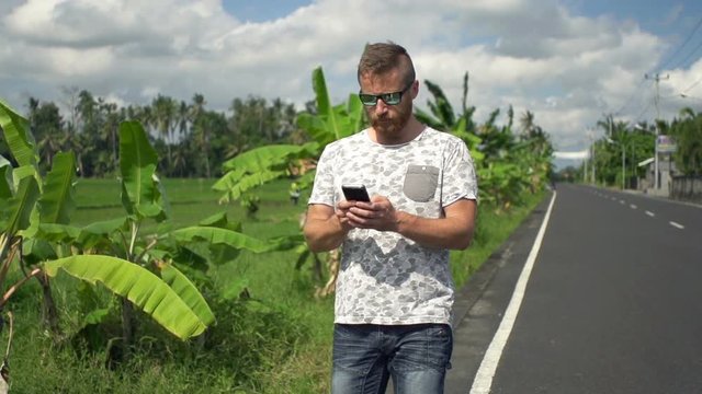 Young man with smartphone walking on road in country, super slow motion 240fps
