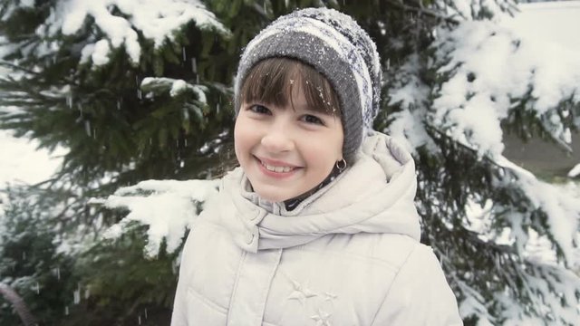 Cute young girl smiling before snowy tree in winter time