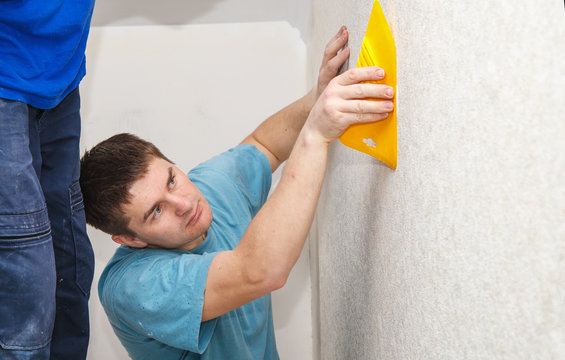 young worker smoothing wallpaper