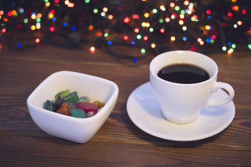 A romantic still life with a cup of freshly brewed coffee and a bowl of candies on a rustic wooden table. Dark blurred bokeh background