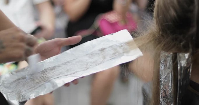 The hairdresser stylist applies the paint on a strand of hair using a brush and foil.