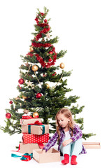 Portrait of little girl unpacking gift boxes near Christmas tree on white background