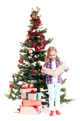 Portrait of cute little girl reading book near Christmas tree on white background
