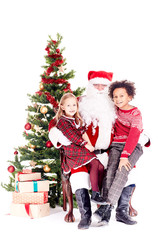 Santa Claus sitting in chair near Christmas tree with multi-ethnic boy and girl on his lap