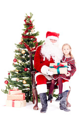 Cute little girl receiving gift from Santa Claus sitting on his lap near Christmas tree