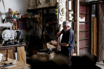 Senior man working on his wooden sculpture in his workshop.
