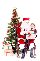 Cute little girl receiving gift from Santa Claus sitting on his lap near Christmas tree