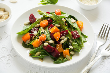 Fresh autumn salad with marinated pumpkin and beetroot, spinach leaves,olive oil, sesame and pumpkin seeds on white table cloth. Space for copy