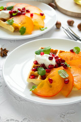 Plates of Belgian waffles with persimmon, pomegranate seeds and sour cream on white table cloth