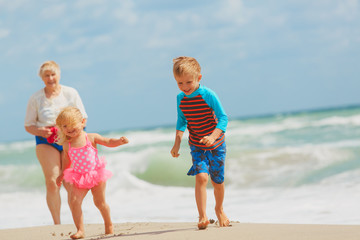 Happy grandmother with kids- little boy and girl- play on beach