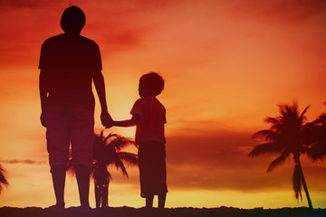 silhouette of father and son holding hands at sunset beach